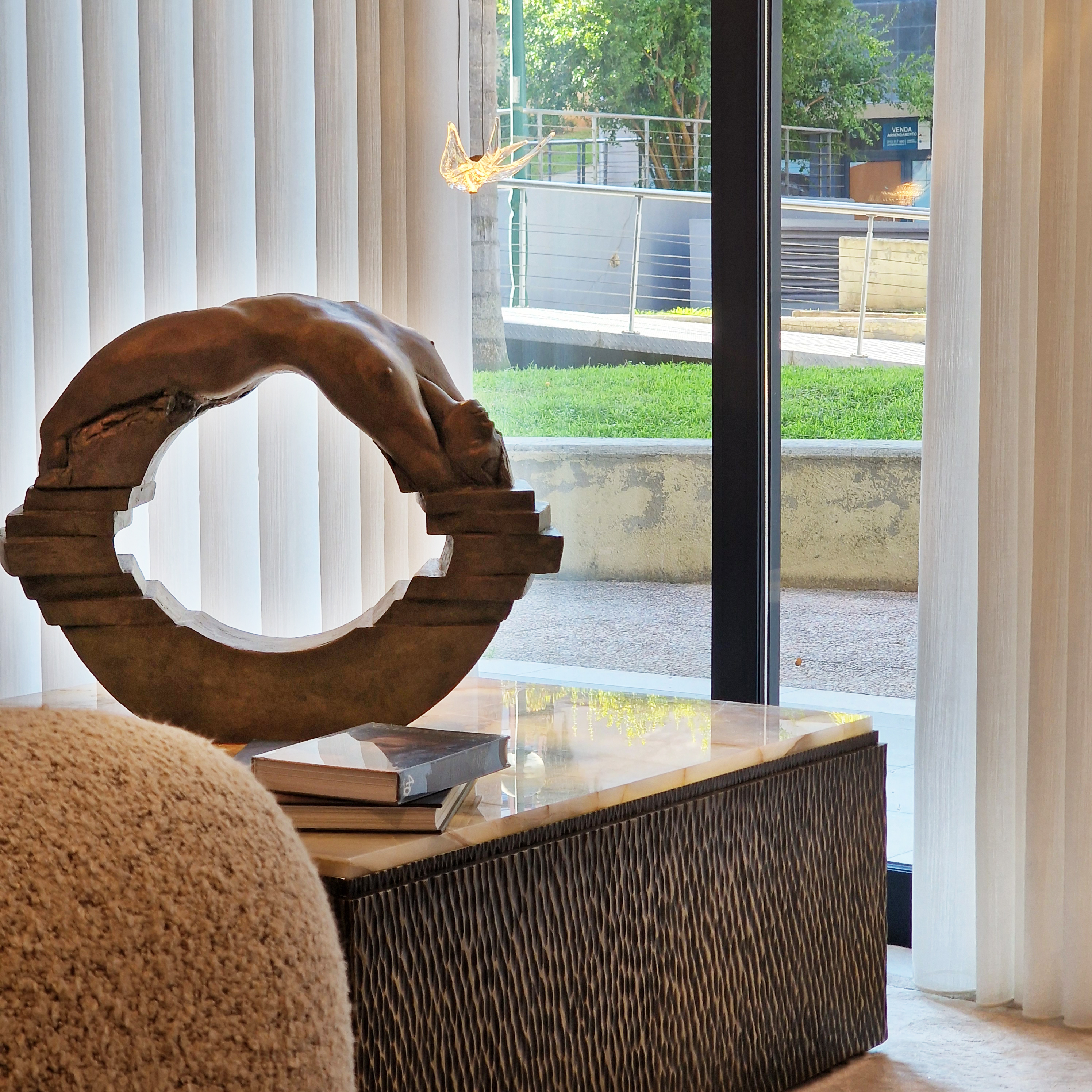 A modern sculpture depicting a figure diving through a circular frame, displayed on a coffee table in a bright interior with large windows and greenery visible outside.