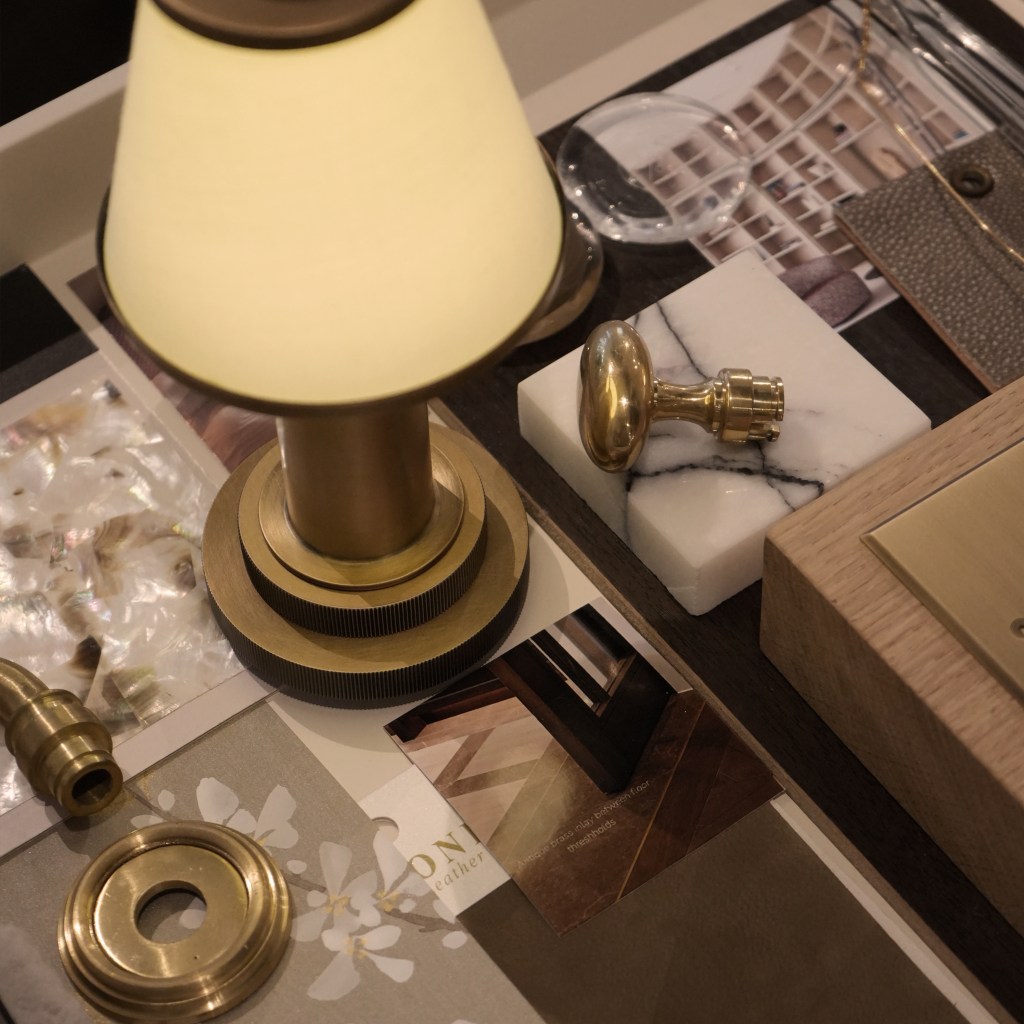A collection of decorative items and materials, including a brass lamp, a marble base, a magnifying glass, and various samples of fabric and textures, arranged on a table.